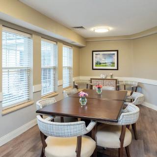 A cozy dining room with a wooden table, surrounded by cushioned chairs, and adorned with flowers and artwork.