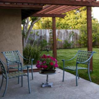 A cozy backyard patio with metal chairs and a small table adorned with a pot of vibrant flowers, surrounded by a lush green lawn.