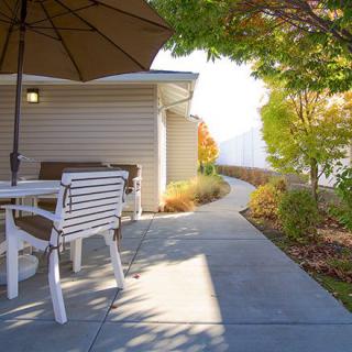 A sunny patio with outdoor furniture and a pathway leading through a landscaped garden.