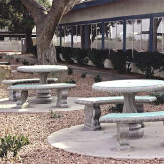 A tranquil outdoor space featuring several concrete picnic tables surrounded by gravel and greenery.