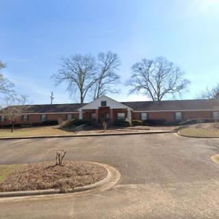 A single-story brick building with a circular driveway and trees in the background.