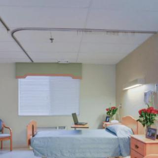 A well-lit hospital room with a bed, flowers on the side table, and a chair near the window.