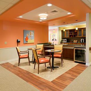 A cozy interior dining area with orange walls, featuring a small kitchenette and wooden furniture.