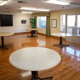An empty room with several round tables and a wooden floor, brightly lit by natural and artificial light.