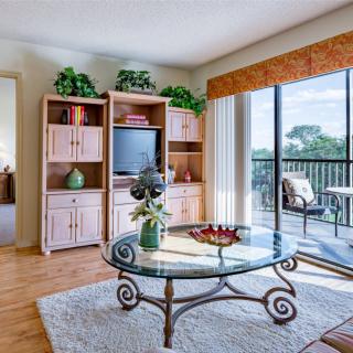 A cozy living room with a glass coffee table, entertainment center, and sliding doors leading to a balcony.