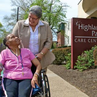 A caregiver assists an elderly woman in a wheelchair outside the Highland Park Carl Center, showcasing compassion and support.