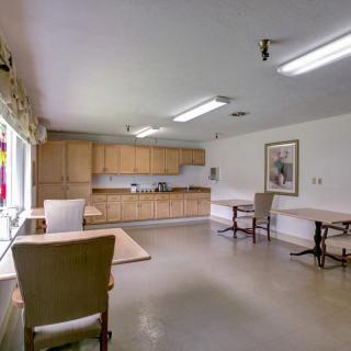A room with a kitchen area, tables, and chairs.