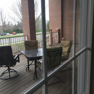 A view of a porch with outdoor chairs and a table seen through a window.