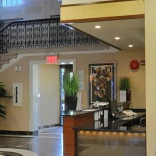A modern lobby interior featuring a reception desk and decorative plants with a staircase in the background.