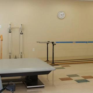 A rehabilitation room equipped with a padded table and parallel bars.
