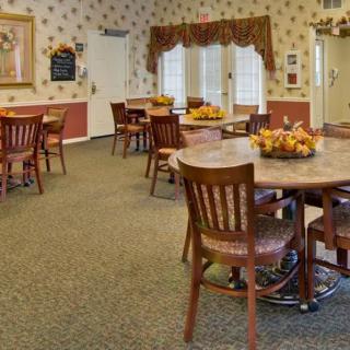 A cozy dining room with tables and chairs, decorated with floral arrangements and warm lighting.