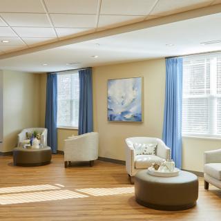 A cozy waiting room featuring comfortable seating, large windows with blue curtains, and a calming piece of artwork on the wall.