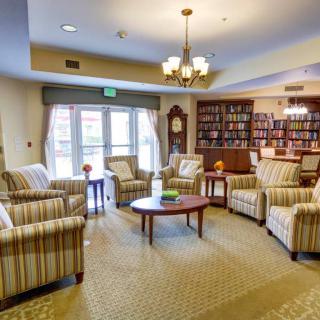 A cozy living room with armchairs and bookshelves, featuring a chandelier and a carpeted floor.