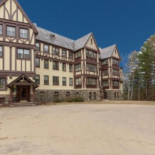 A historic Tudor-style building surrounded by trees under a clear blue sky.