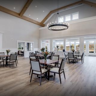 A spacious and bright dining area with multiple tables and chairs, featuring a large chandelier and wooden flooring.