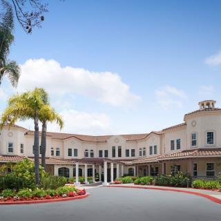 A two-story building with a manicured entrance, surrounded by palm trees and gardens under a clear blue sky.
