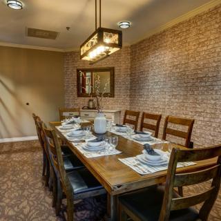 A cozy dining room with a wooden table set for a meal, featuring brick walls and a warm chandelier.