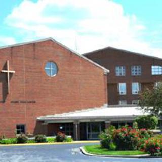 A brick church building with a prominent cross and surrounding landscape.