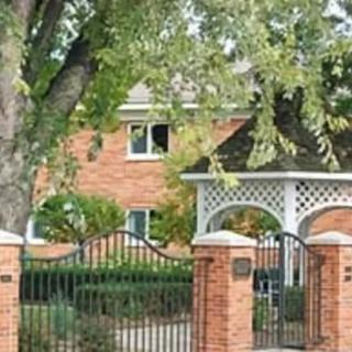 Brick house with a gated entrance surrounded by lush trees and greenery.