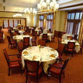 An elegant dining room setup with neatly arranged tables and chairs, illuminated by chandeliers.