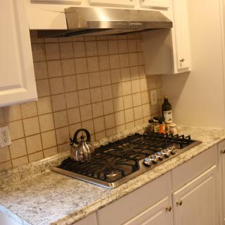 A kitchen setup featuring a gas cooktop with a kettle, tiled backsplash, and white cabinets.