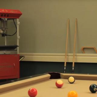 A recreation room featuring a pool table with balls and cue sticks, alongside a popcorn machine.