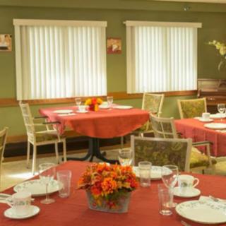 A cozy dining room with neatly set tables, adorned with floral centerpieces and surrounded by chairs.