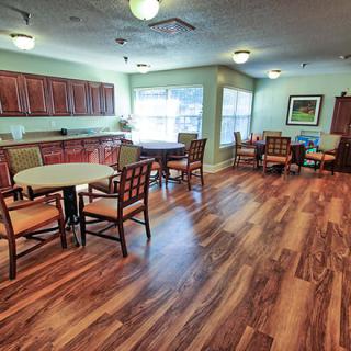A cozy dining area with round tables and chairs, featuring a wooden floor and adjacent kitchen space.