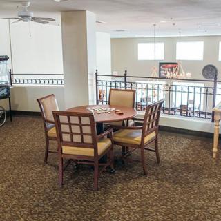 A cozy indoor area with a wooden table and chairs on a carpeted floor, featuring a ceiling fan and railing.