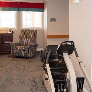A room with exercise equipment and a comfortable chair near the windows.
