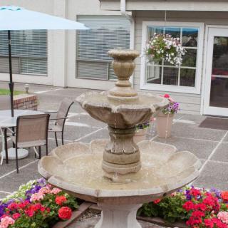 A decorative fountain surrounded by colorful flowers on a patio with seating and umbrellas.