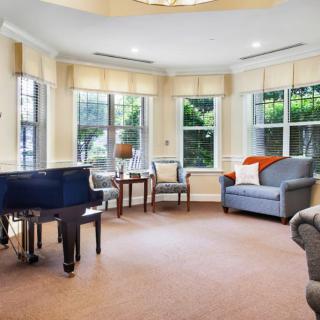 A cozy living room featuring a grand piano, sofas, chairs, and large windows allowing in plenty of natural light.