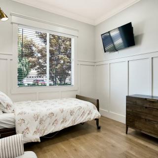 A modern bedroom with a single bed, wall-mounted TV, and a large window providing natural light.
