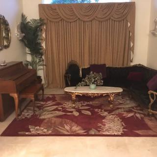 A warmly decorated living room featuring a grand piano, plush sofa, and ornate rug.