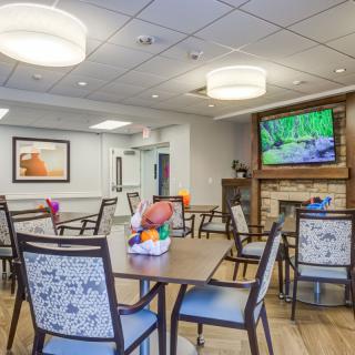 A modern dining area with tables and chairs, featuring a large TV and decorative elements.