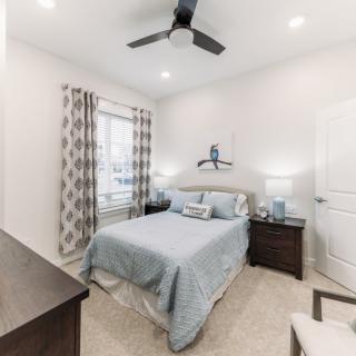A modern bedroom featuring a double bed with light blue bedding, flanked by two nightstands and lamps. The room is decorated with patterned curtains and has a ceiling fan.