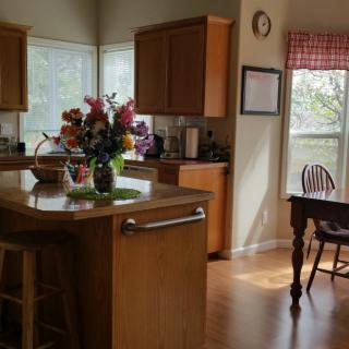 A cozy kitchen with wooden cabinets, an island adorned with a bouquet of flowers, and natural light streaming in.