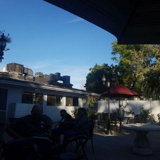 A peaceful patio scene with chairs, an umbrella, and a building in the background under a clear blue sky.