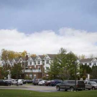 A view of a building with a parking lot in front, surrounded by trees under a cloudy sky.