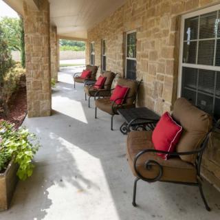 A cozy porch with comfortable chairs and red cushions lined up against a stone wall, complemented by potted plants.