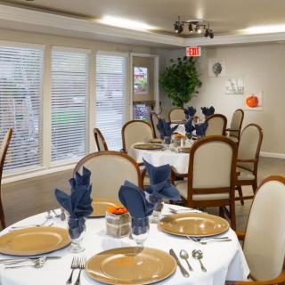 An elegantly set dining room with tables prepared for guests, featuring blue napkins and arranged silverware.