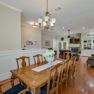 A spacious dining room with a wooden table and chairs, featuring a decorative chandelier and hardwood flooring, seamlessly connected to the kitchen.