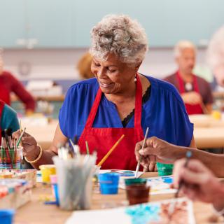 A group of senior adults enjoying a painting class together, using brushes and colorful paints.
