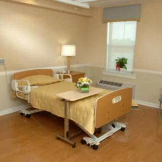 A clean and neatly arranged hospital room with a single bed, bedside table, and window.