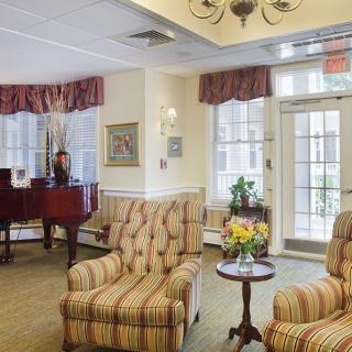 A cozy living room with armchairs and a piano by the windows.