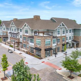A modern residential apartment complex with a brick and siding exterior, situated on a tree-lined urban street.