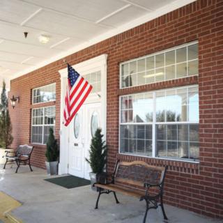 A brick building with an American flag, benches, and potted plants by the entrance.