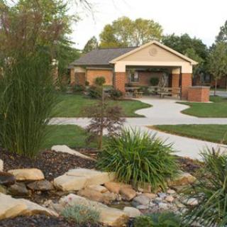 A beautifully landscaped garden with a small house in the background, featuring lush greenery and winding pathways.