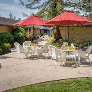 A sunny patio with tables, chairs, and red umbrellas set in a garden.