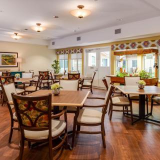 A cozy dining room with neatly arranged tables and chairs, illuminated by ample natural light.
